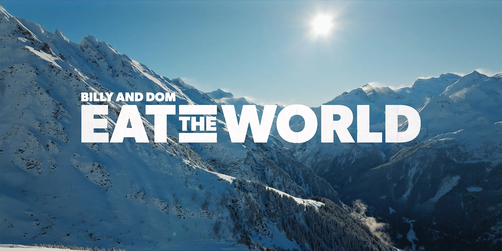 Snow-covered Alpine peaks under a bright sun, with the title Billy and Dom Eat The World